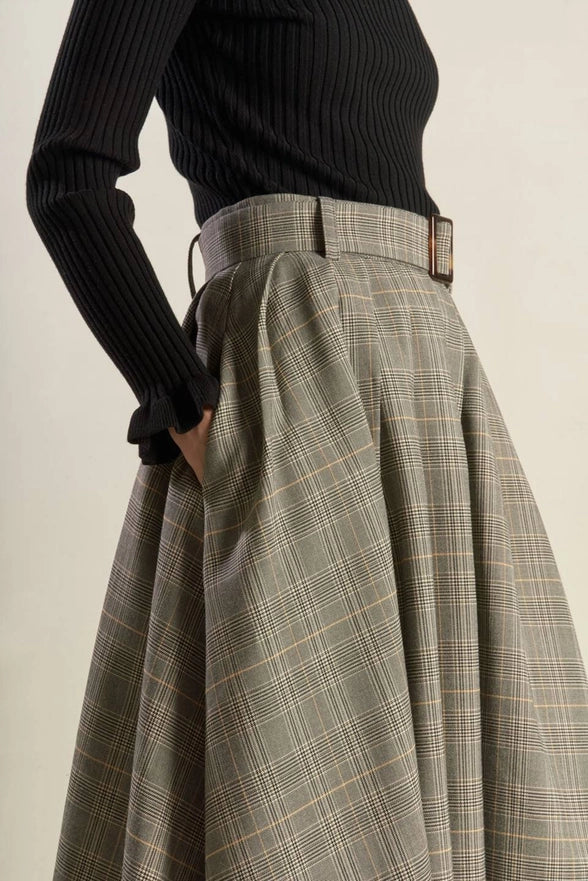 Person wearing a black ribbed sweater and plaid skirt on a plain background