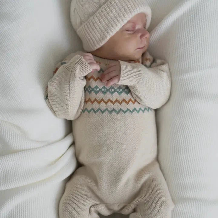 Newborn baby wearing a knitted hat and a onesie with a pattern, lying on a white surface.