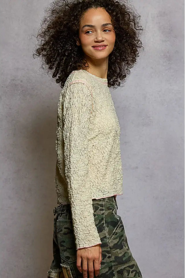 Woman wearing a textured long-sleeve top and camouflage pants against a gray background