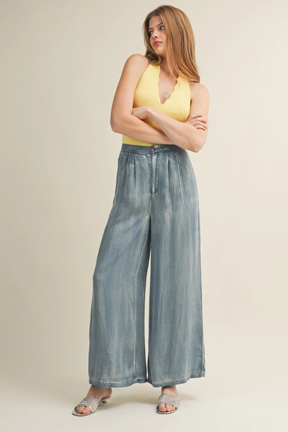 Woman wearing a yellow top and wide-leg jeans on a beige background