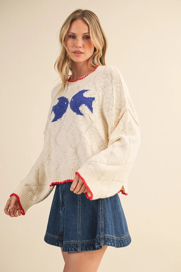 Woman wearing a cream sweater with blue fish design and denim skirt on a beige background