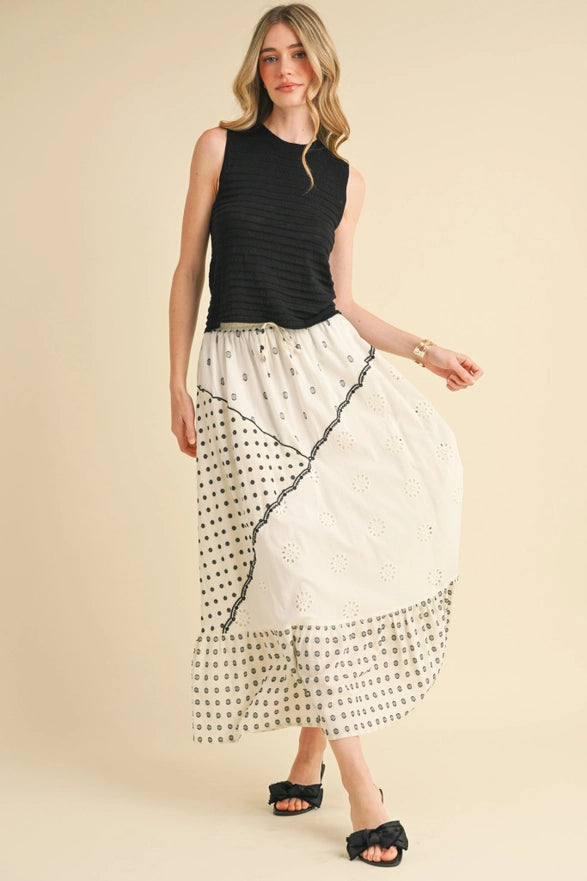 Woman wearing a black sleeveless top and a long, patterned skirt on a beige background