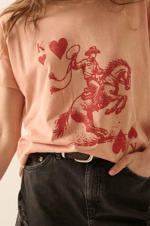 Person wearing a light pink t-shirt with a red graphic of a cowboy on a horse and hearts.