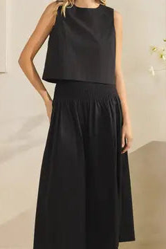 Woman wearing a black sleeveless top and skirt set against a neutral background