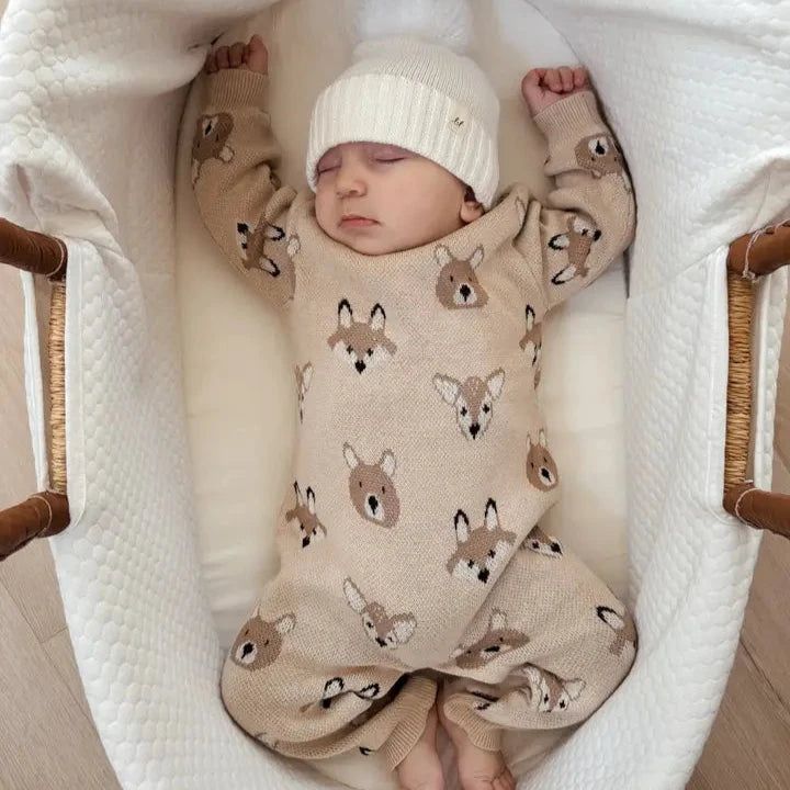 Baby in a crib wearing a fox-patterned outfit and white hat.