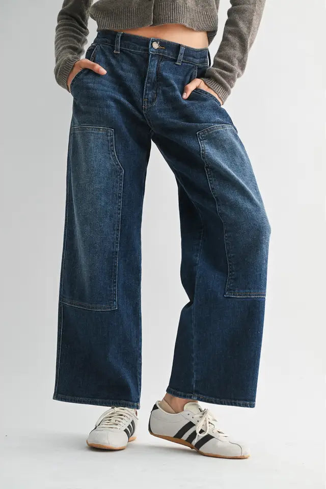 Person wearing wide-leg jeans and Adidas sneakers on a plain background