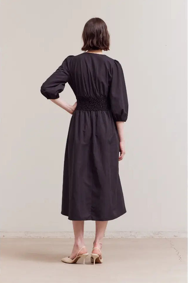 Woman wearing a black dress standing against a plain background