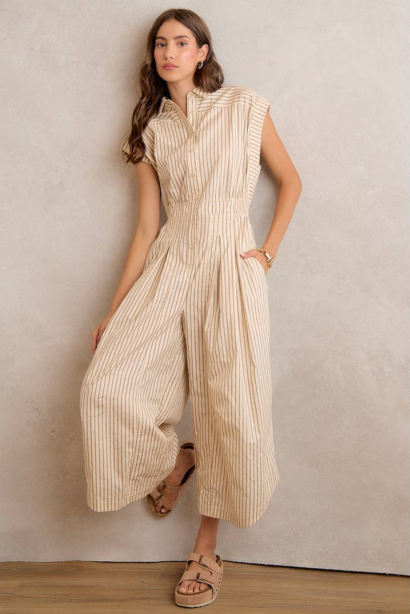 Woman wearing a beige striped jumpsuit against a plain wall.