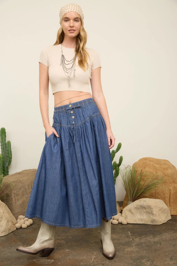 Woman wearing a blue denim skirt and beige top in a desert-themed setting