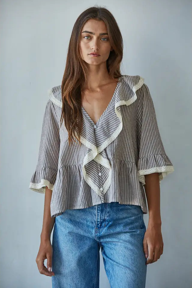Woman wearing a striped blouse with ruffled details and blue jeans against a plain background