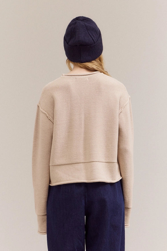 Person wearing a beige sweater and navy pants with a navy beanie on a plain background