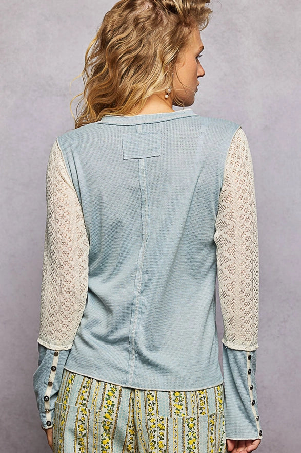 Woman wearing a light blue vest with lace sleeves on a gray background