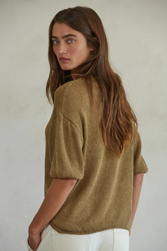Woman wearing a mustard yellow knitted sweater against a plain background