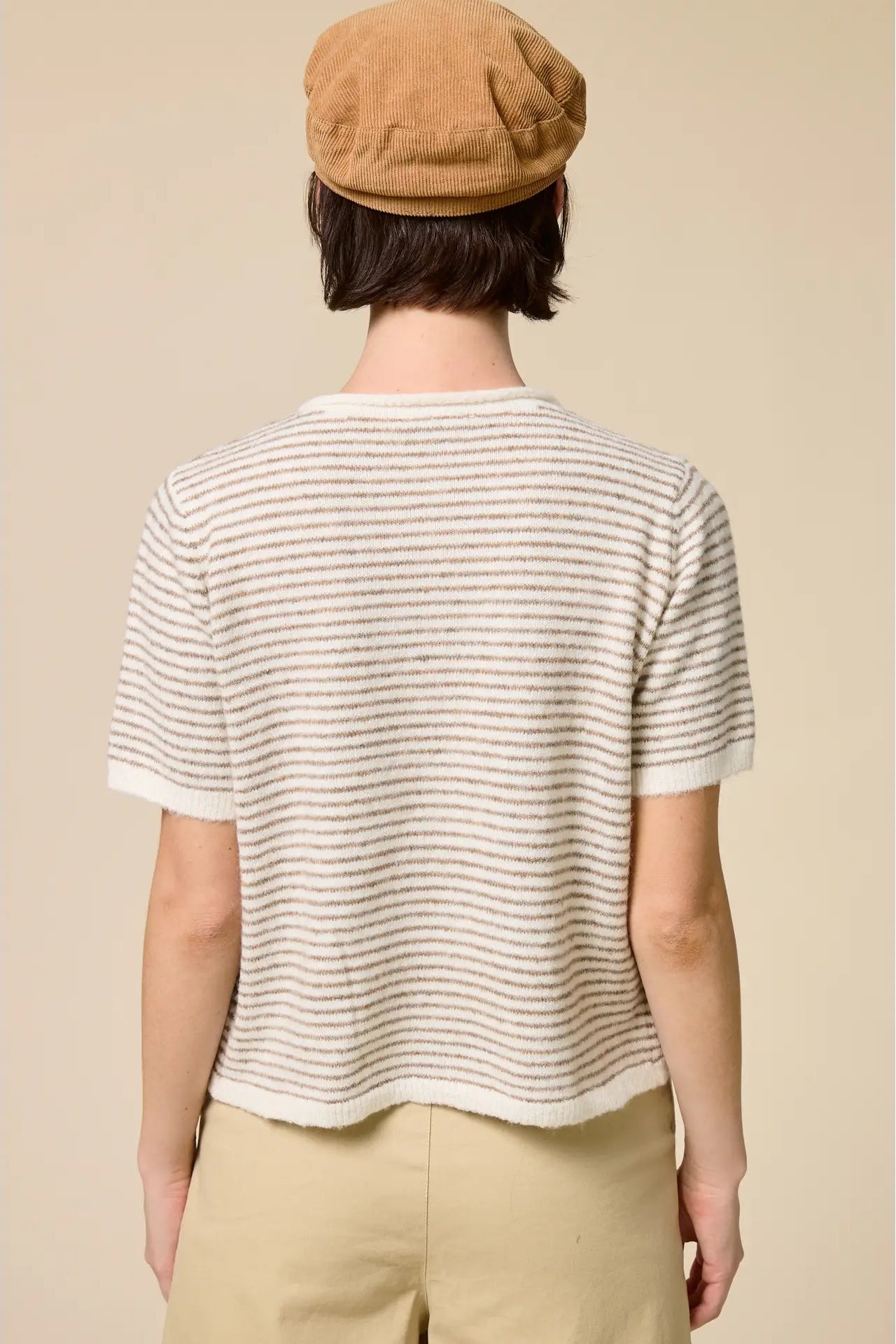 Person wearing a striped shirt and beige cap on a plain background