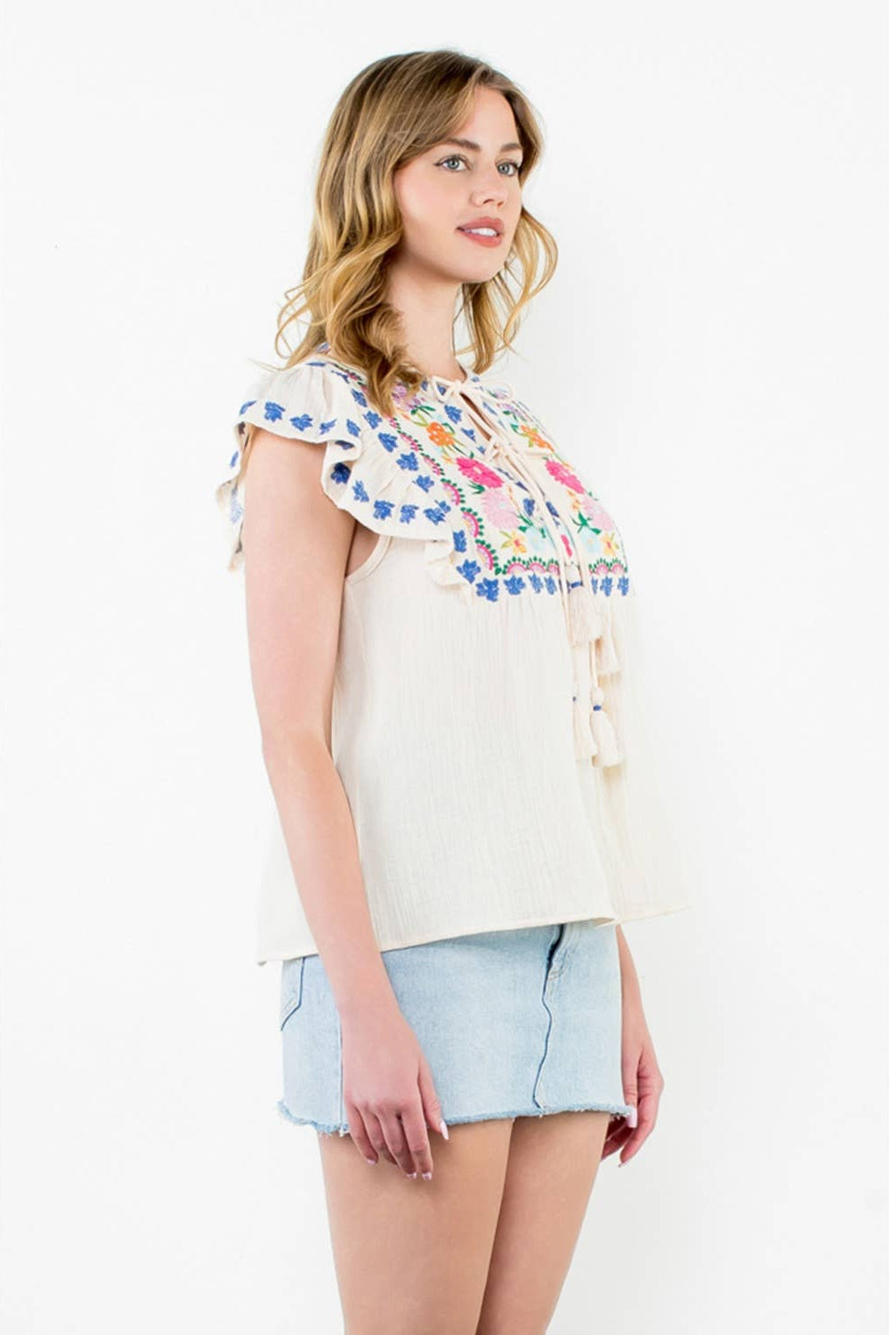 Woman wearing a colorful floral top and denim shorts on a white background
