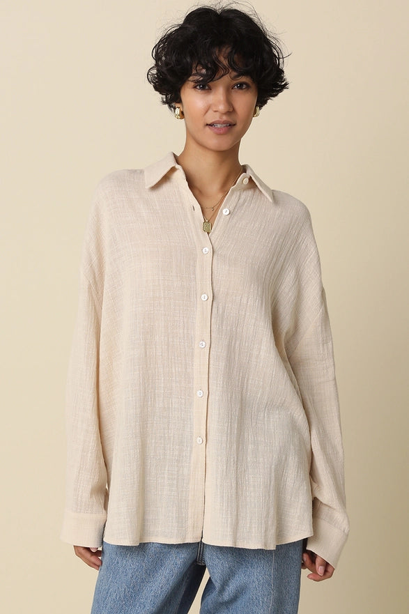 Woman wearing a beige button-up shirt and blue pants against a beige background