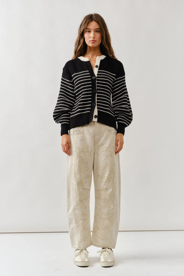 Person wearing a black and white striped cardigan with beige pants on a white background