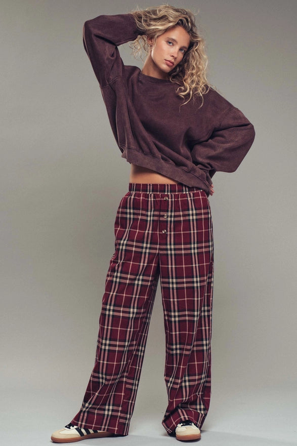 Woman wearing a maroon sweater and plaid pants against a plain background