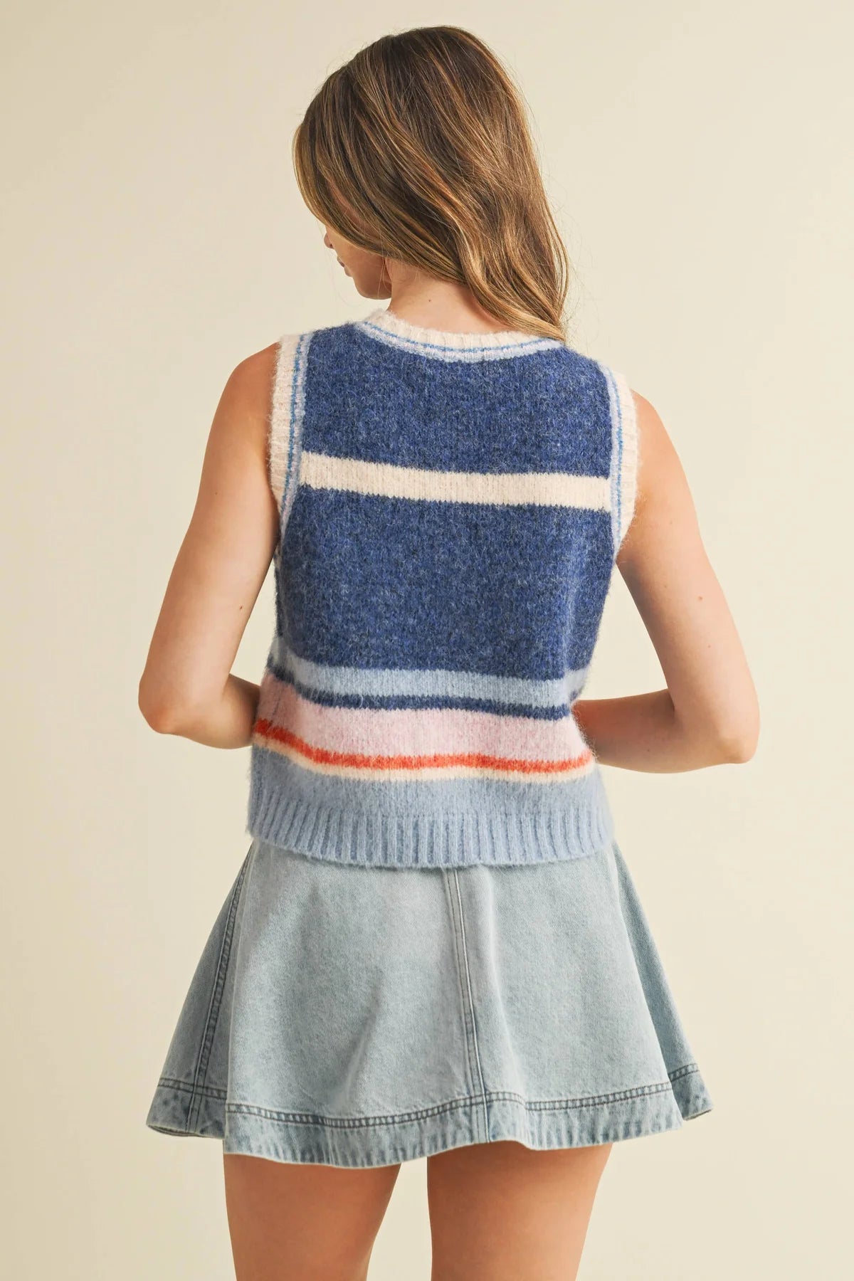 Woman wearing a colorful striped sweater vest over a denim dress on a beige background