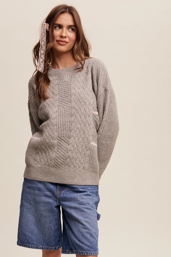 Woman standing against a plain background wearing a heather grey pull over sweater