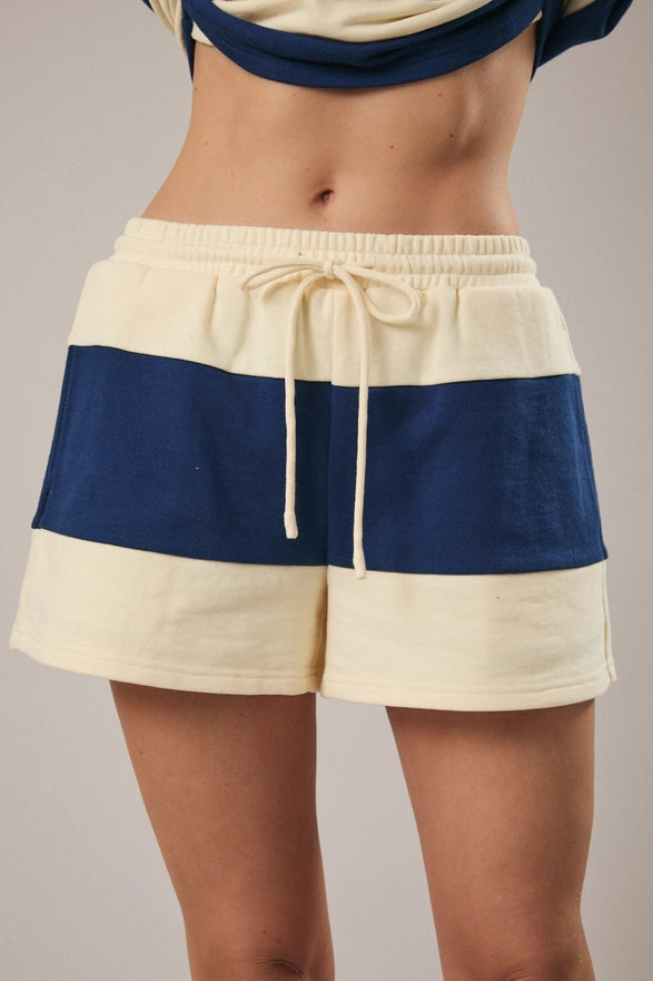 Model is wearing a matching cream and navy striped set with shorts and a half zip polo like top.