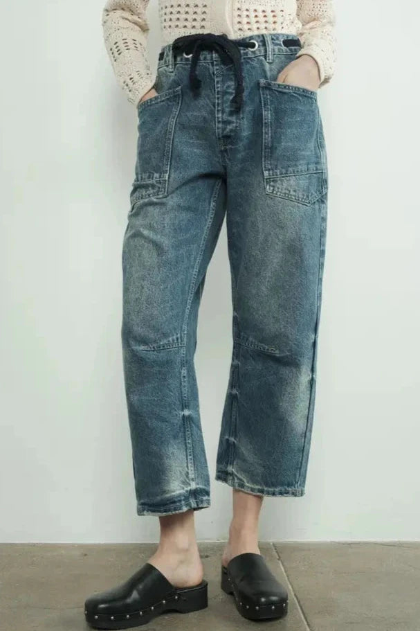 Person wearing blue jeans and black clogs on a plain background