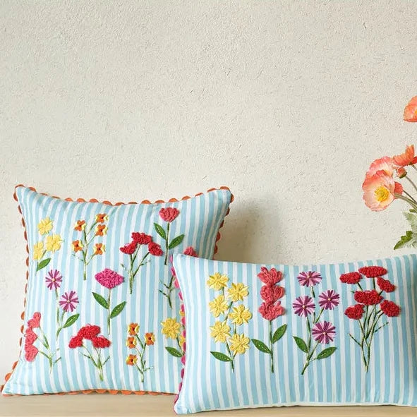 Two decorative pillows with floral patterns on a wooden surface with a vase of flowers in the background.