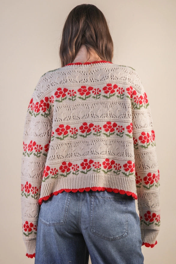 Person wearing a floral-patterned sweater with red flowers on a plain background