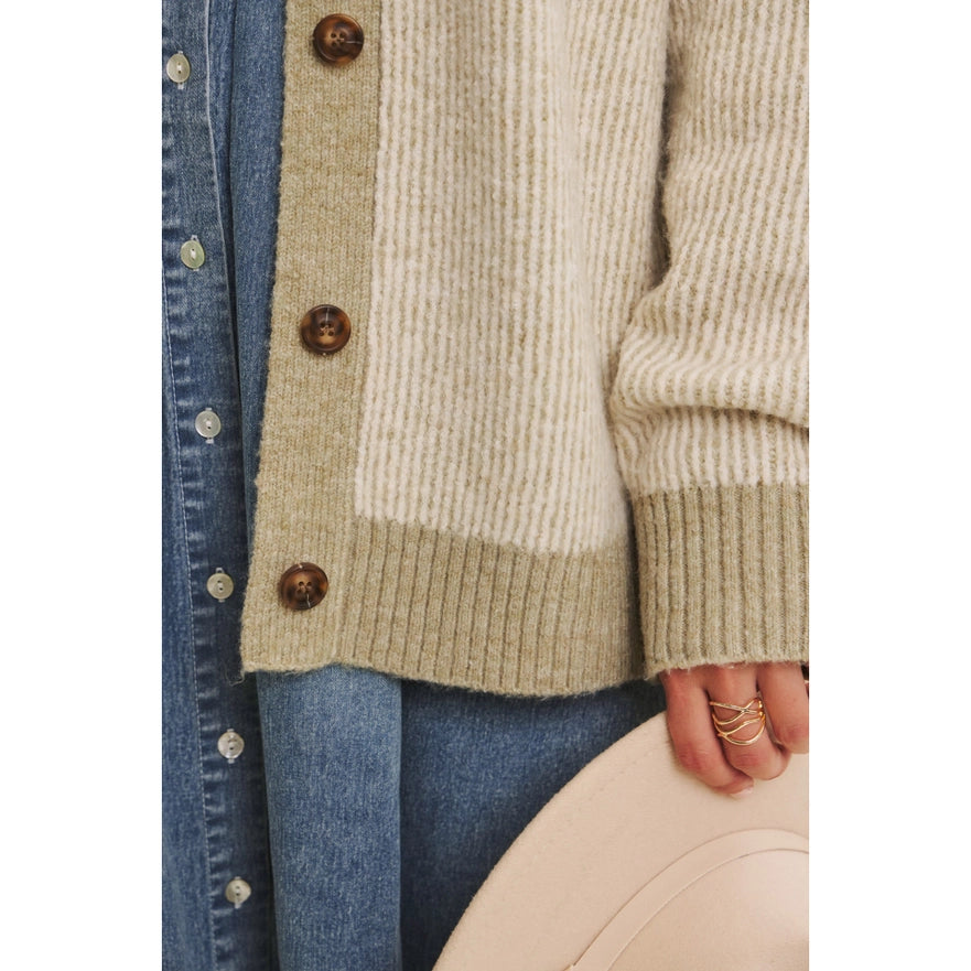 Close-up of a person wearing a beige ribbed sweater over a denim jacket.
