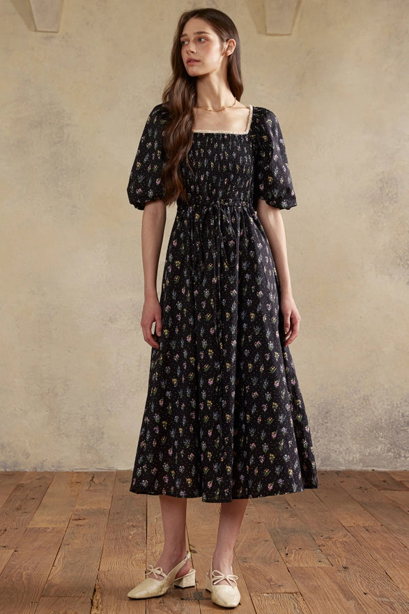 Woman wearing a black floral dress standing against a beige wall.