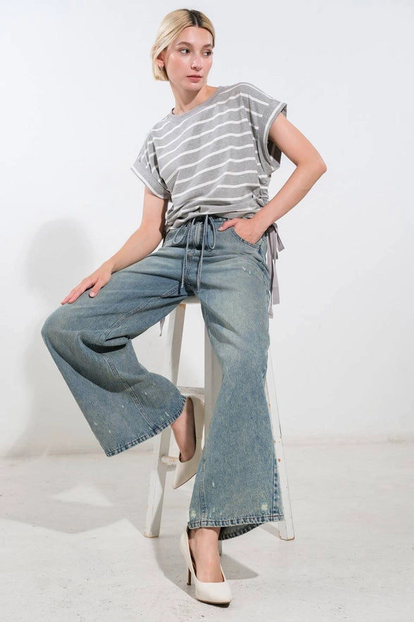 Woman wearing a striped shirt and wide-leg jeans sitting on a stool against a white background