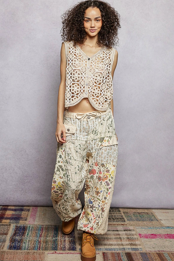 Woman wearing a patterned outfit with a textured vest and floral pants on a plain background