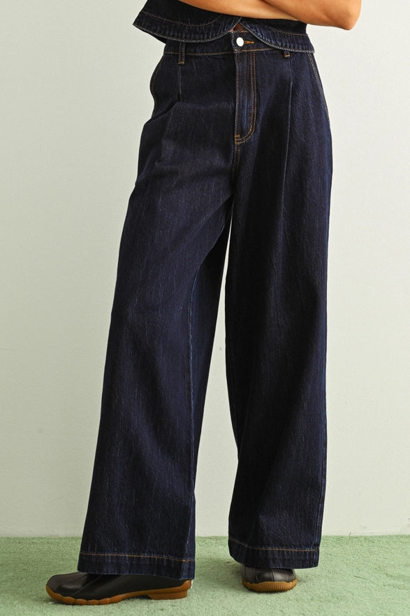 Person wearing dark blue wide-leg jeans on a light green background