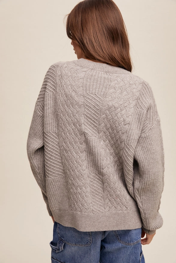 Woman standing against a plain background wearing a heather grey pull over sweater