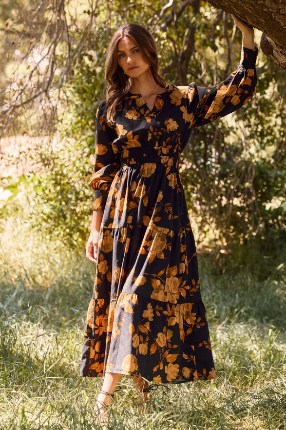 Woman in a floral dress standing in a natural setting with trees and grass.