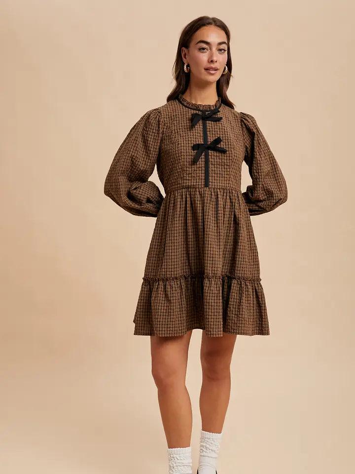 Woman wearing a brown checkered dress with long sleeves and a black bow on a beige background