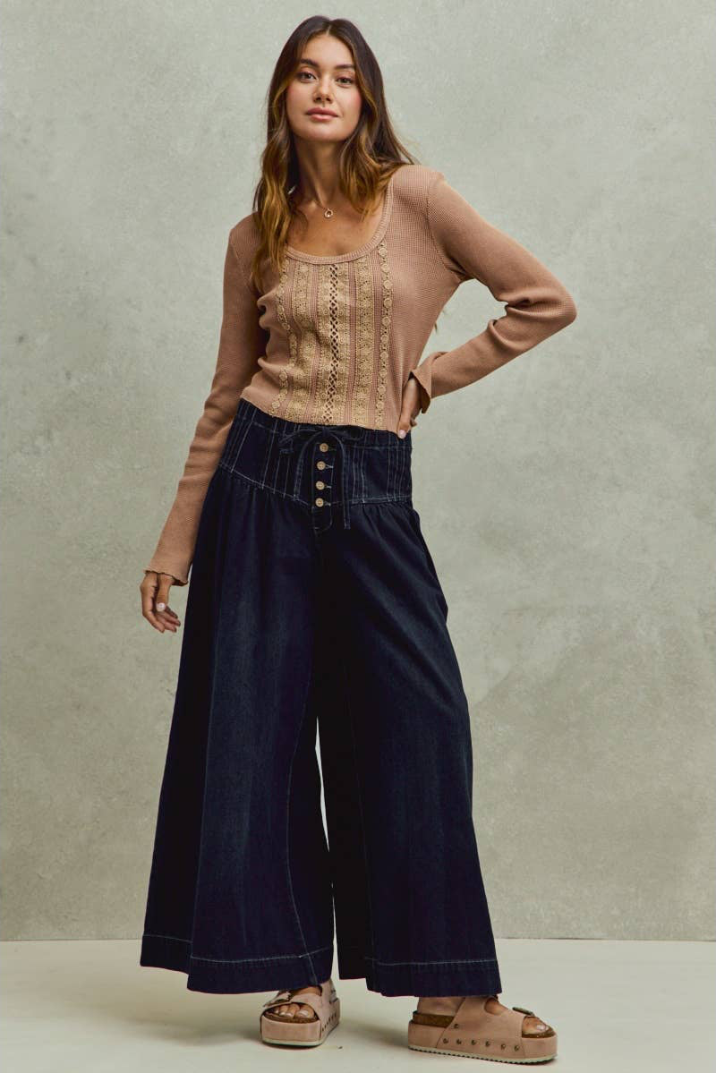 Woman wearing a beige sweater and dark blue wide-leg pants against a neutral background