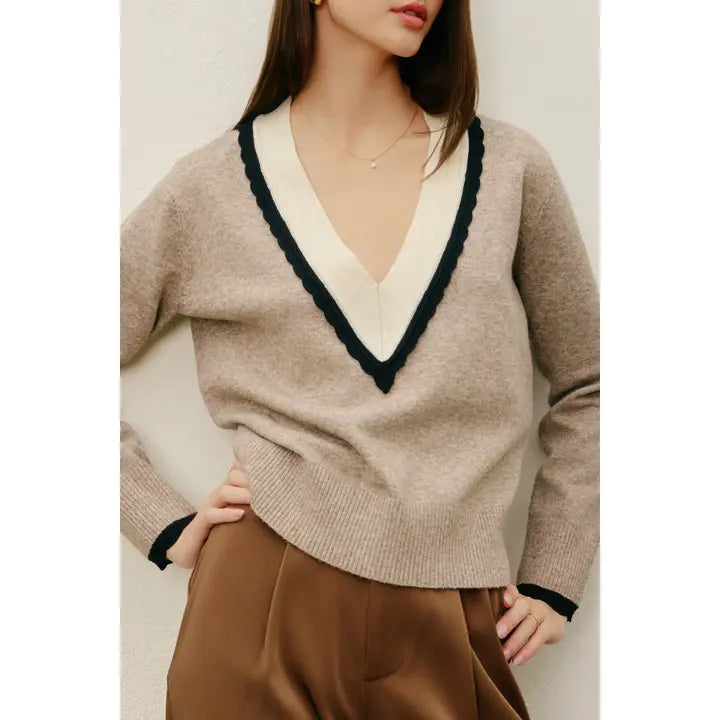 Beige sweater with black trim worn by a person against a neutral background