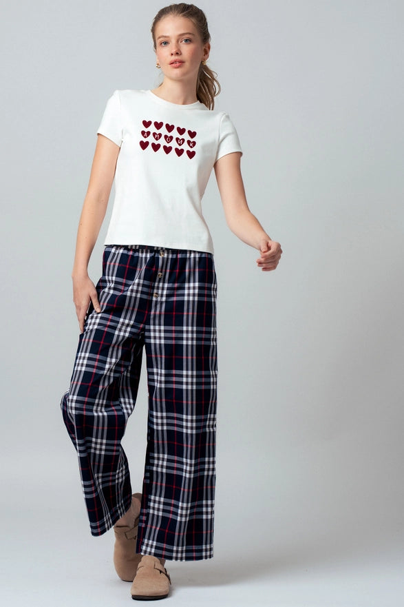 Woman wearing a white t-shirt with red heart patterns and plaid pants on a gray background