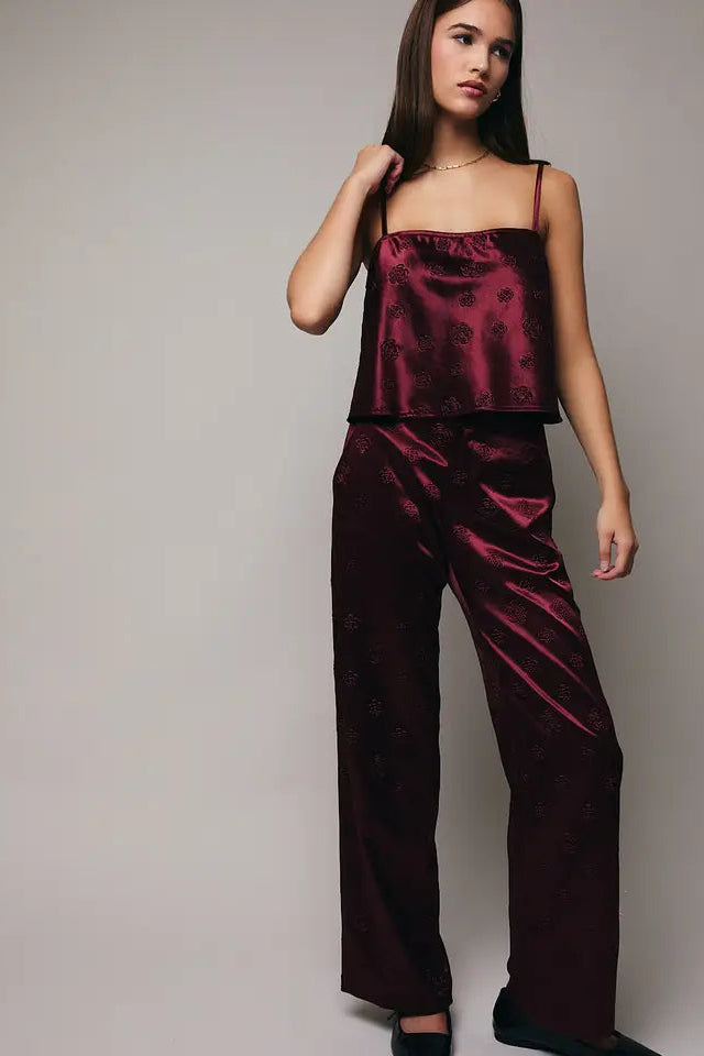 Woman wearing a burgundy satin pajama set against a plain background