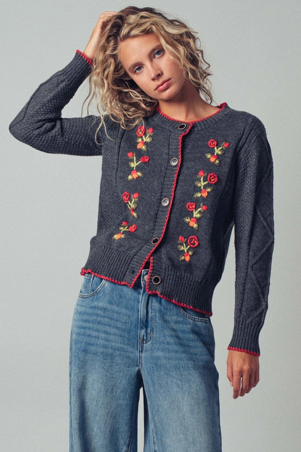 Woman wearing a dark blue cardigan with floral embroidery on a gray background