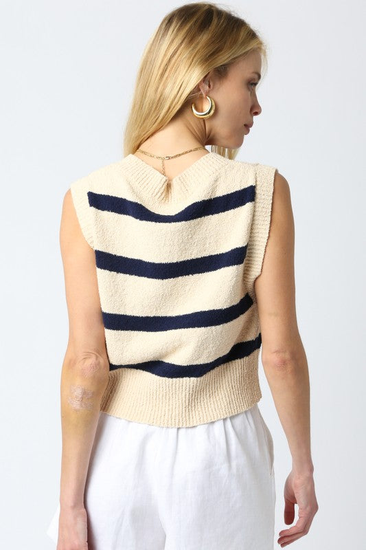Woman wearing a beige sleeveless sweater with navy stripes on a white background