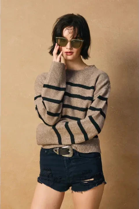 Woman wearing a striped sweater and denim shorts against a beige background