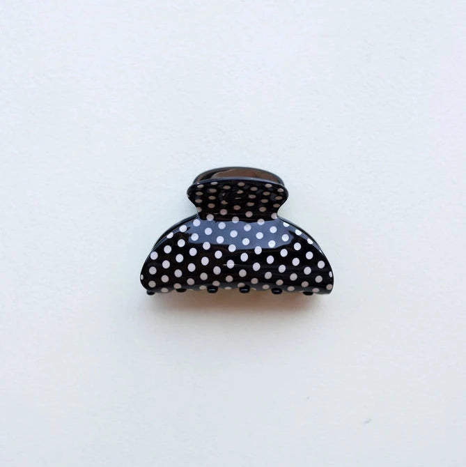 Black hair clip with white polka dots on a light gray background