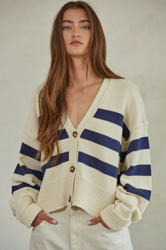 Woman wearing a cream and navy striped cardigan against a plain background