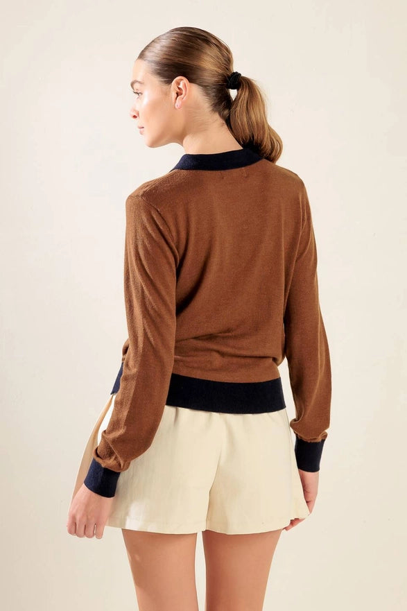 Woman wearing a brown sweater and beige shorts against a plain background