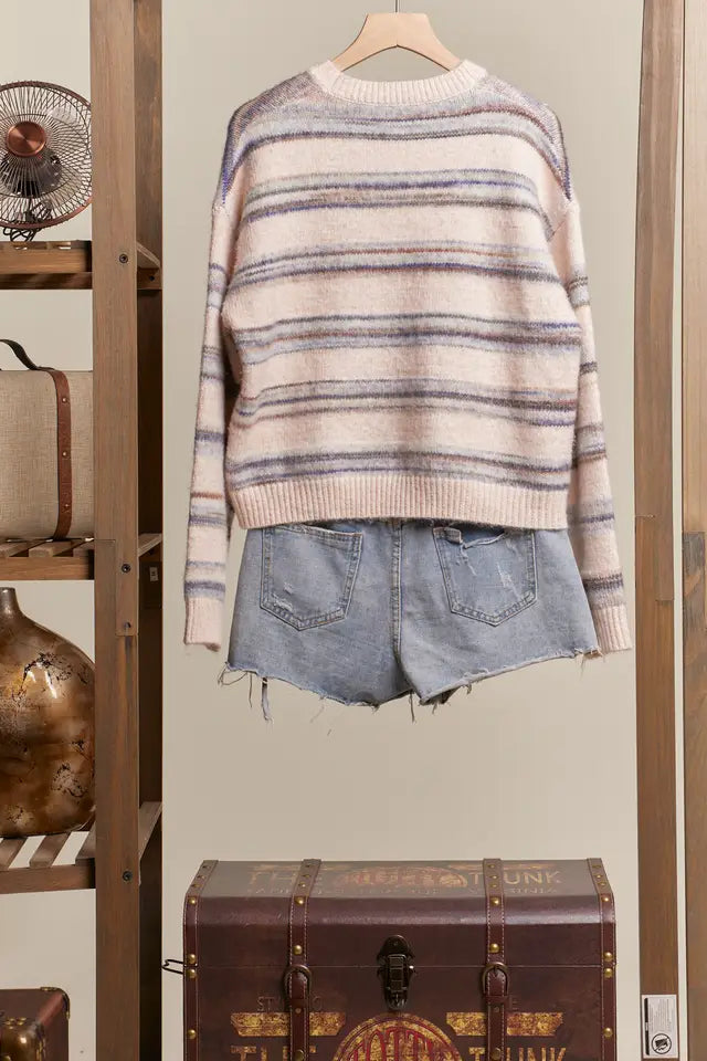 Striped sweater and denim shorts on a hanger against a neutral wall with vintage items.