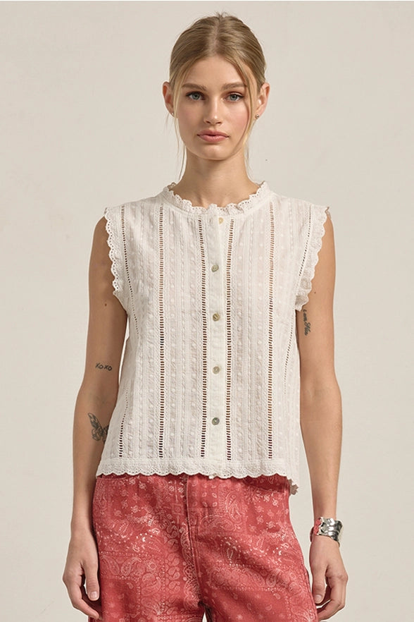 Woman wearing a white sleeveless top with lace details and red pants on a beige background