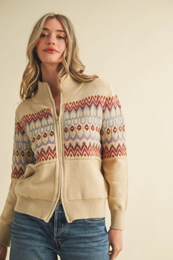 Woman wearing a beige sweater with a colorful pattern on a plain background