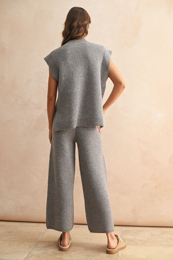 Woman wearing a gray sleeveless top and wide-leg pants against a beige wall.